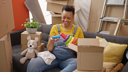 Young pregnant woman unpacking toys and clothes of cardboard box at new home