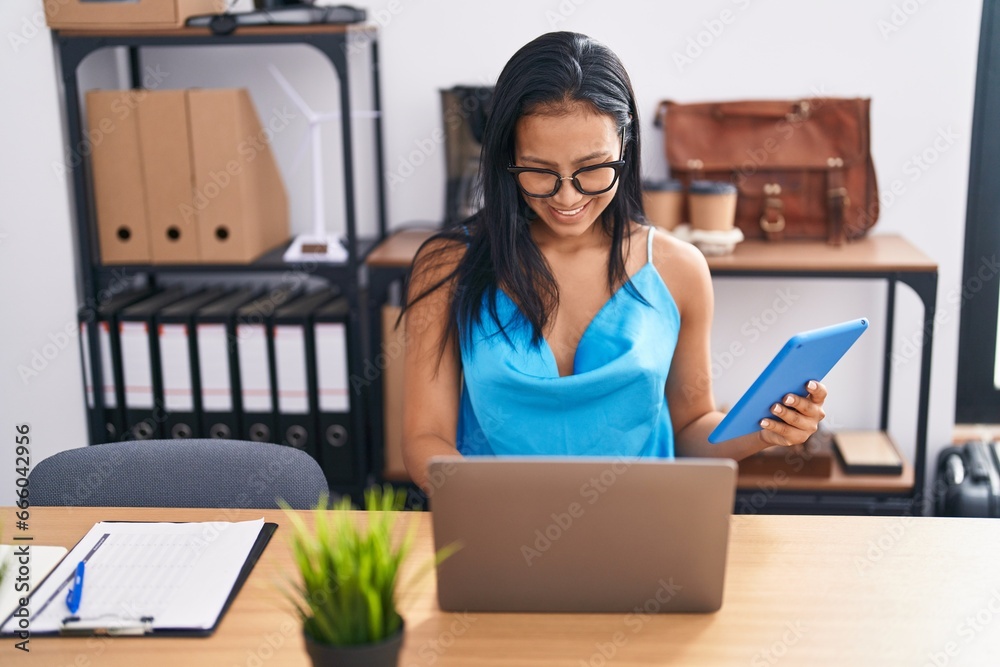 Wall mural Young beautiful latin woman business worker using touchpad and laptop at office