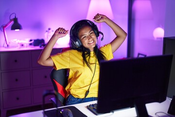 Fototapeta na wymiar Young beautiful latin woman streamer playing video game with winner expression at gaming room