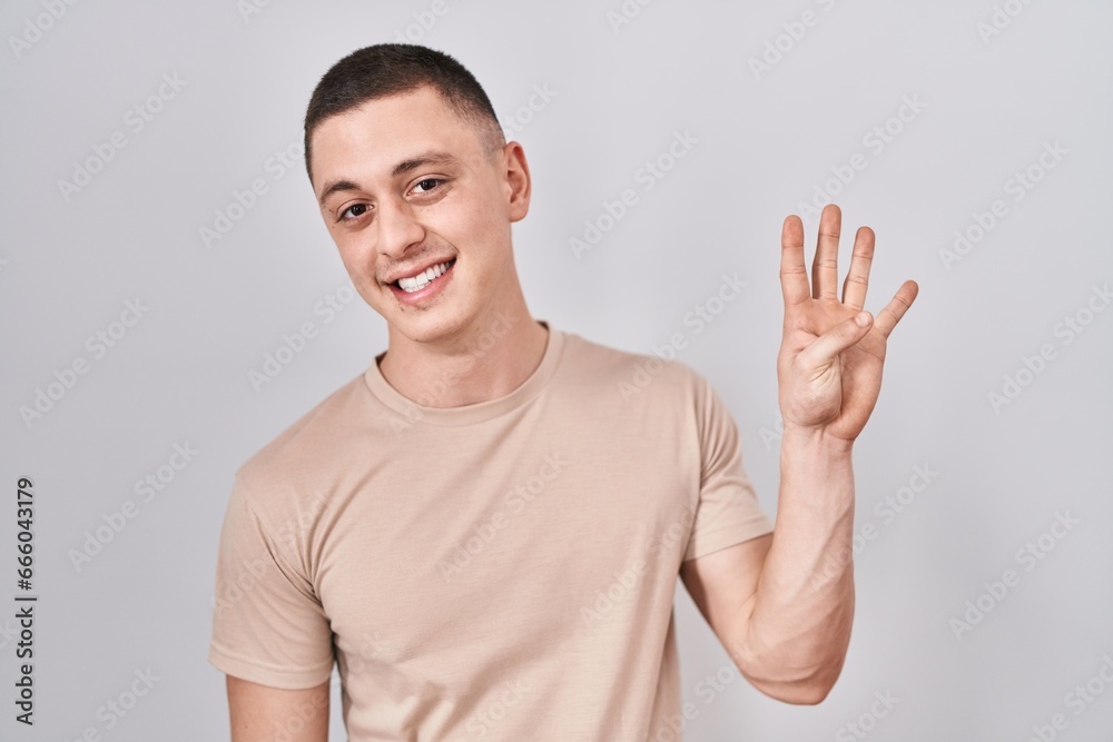 Wall mural Young man standing over isolated background showing and pointing up with fingers number four while smiling confident and happy.