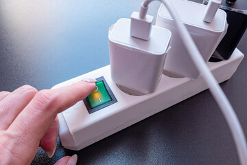 Hand pressing the power button on multiple socket outlet before leaving the house. Turn off, when...