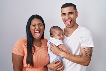 Young hispanic couple with baby standing together over isolated background sticking tongue out happy with funny expression. emotion concept.