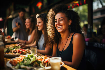 Joyful woman laughing heartily while dining outdoors with friends, capturing a warm, sunlit moment of togetherness.