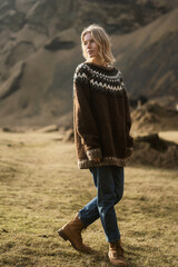 A girl in fashion clothes poses in mountains an Icelandic sweater