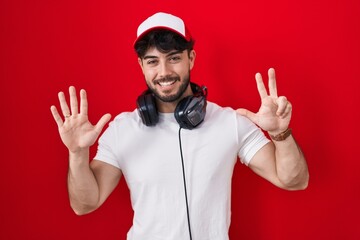Naklejka premium Hispanic man with beard wearing gamer hat and headphones showing and pointing up with fingers number eight while smiling confident and happy.