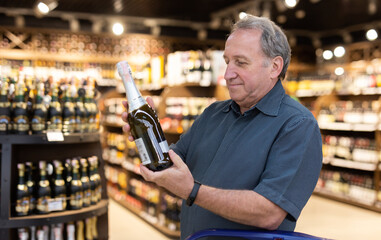 Mature man choosing fine bottle of champagne in supermarket