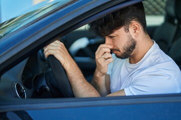 Young hispanic man driving car smelling bad smell at street - obrazy, fototapety, plakaty