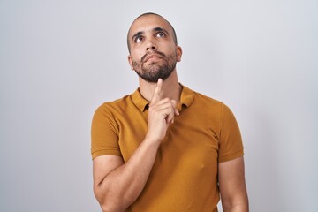 Hispanic man with beard standing over white background thinking concentrated about doubt with...