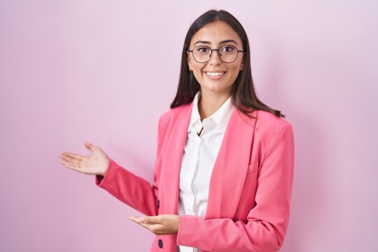 Young hispanic woman wearing business clothes and glasses inviting to enter smiling natural with open hand