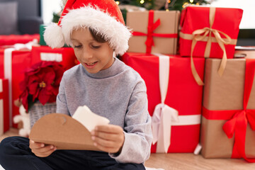 Obraz na płótnie Canvas Adorable hispanic boy putting santa claus letter in envelope sitting by christmas tree at home
