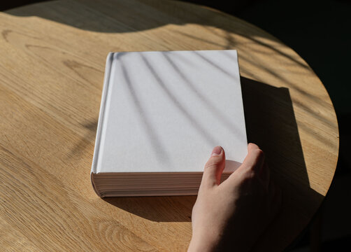 Book cover mockup on wood table. Hand holding literature mock up