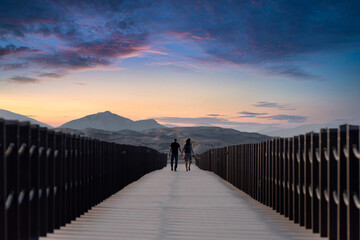 young Couple walking togathar back view on the wood bridge thakira purple island Qatar. No face