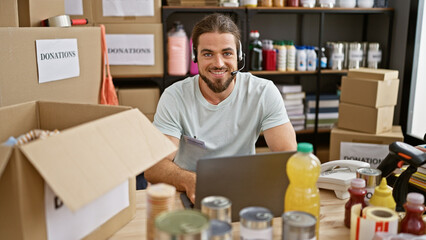 Young hispanic man volunteer using laptop and headphones smiling at charity center