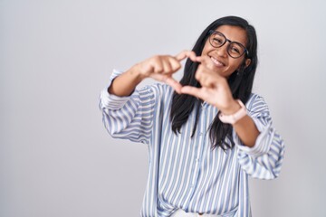 Young hispanic woman wearing glasses smiling in love doing heart symbol shape with hands. romantic...