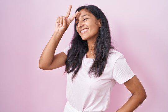 Young hispanic woman standing over pink background smiling looking to the camera showing fingers doing victory sign. number two.