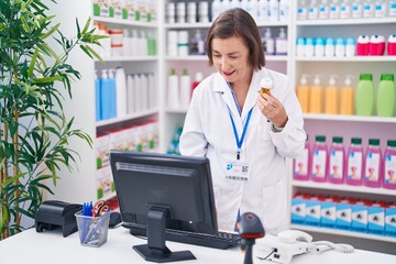 Middle age woman pharmacist using computer holding pills bottle at pharmacy