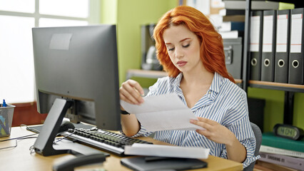Obraz na płótnie Canvas Young redhead woman business worker using computer reading letter at office