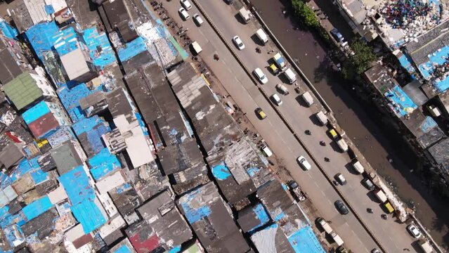 Aerial rooftop view of shanty slums in Dharavi, Mumbai India revealing downtown Mumbai with high rise towers and skyscrapers showing contrast in rich and poor with local railway train passing. 
