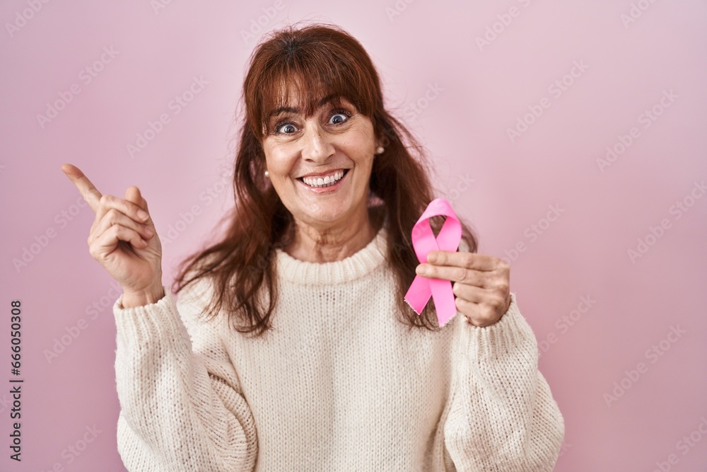 Sticker middle age hispanic woman holding pink cancer ribbon smiling happy pointing with hand and finger to 