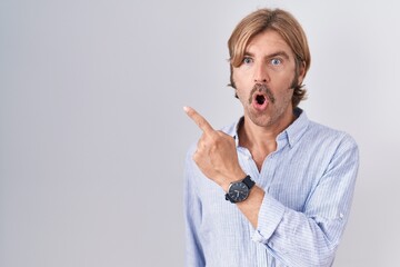 Caucasian man with mustache standing over white background surprised pointing with finger to the side, open mouth amazed expression.