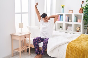 Young hispanic man waking up stretching arms at bedroom