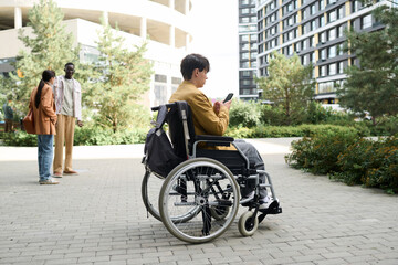 Obraz premium Man sitting in wheelchair and using smartphone during his walk in the city