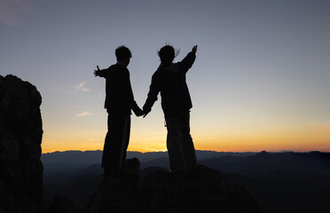 Silhouettes of a Christian man and woman spreading their arms to ask for blessings on a mountain....