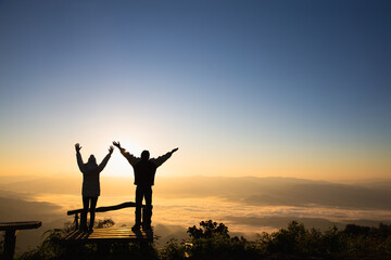 Silhouettes of a Christian man and woman spreading their arms to ask for blessings on a mountain. Together for recovery, providing emotional support. Praying for love and faith in religion. - obrazy, fototapety, plakaty