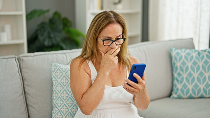 Middle age hispanic woman sitting on sofa using smartphone looking upset at home
