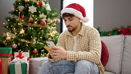 Young arab man using smartphone sitting by christmas tree at home