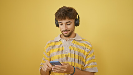 Cool young arab man, with sleek beard, seriously immersed in texting and tuning into music, using...