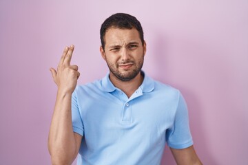 Hispanic man standing over pink background shooting and killing oneself pointing hand and fingers to head like gun, suicide gesture.