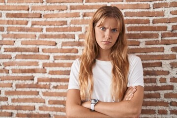 Fototapeta na wymiar Young caucasian woman standing over bricks wall skeptic and nervous, disapproving expression on face with crossed arms. negative person.