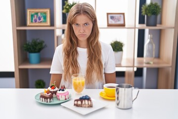 Young caucasian woman eating pastries t for breakfast skeptic and nervous, frowning upset because...