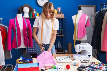 Young blonde girl tailor cutting cloth at sewing studio