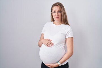 Young pregnant woman expecting a baby, touching pregnant belly skeptic and nervous, frowning upset...
