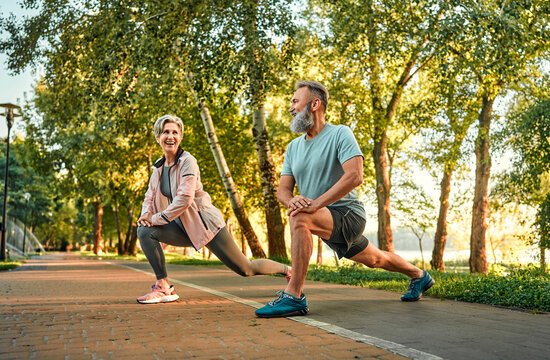 Outdoor exercising on retirement. Motivated aged people spending time in park and doing inverted lunges exercise for training glute and leg muscles. Active athletes making step forward and squatting. - Powered by Adobe
