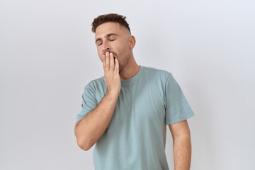 Hispanic man with beard standing over white background bored yawning tired covering mouth with hand. restless and sleepiness.