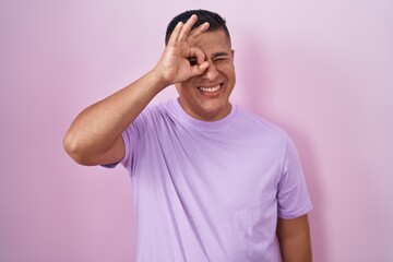 Fototapeta na wymiar Young hispanic man standing over pink background doing ok gesture with hand smiling, eye looking through fingers with happy face.