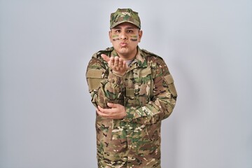 Hispanic young man wearing camouflage army uniform looking at the camera blowing a kiss with hand on air being lovely and sexy. love expression.