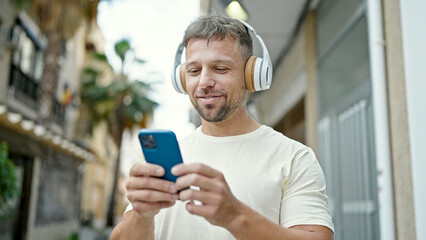 Young man using smartphone wearing headphones at street