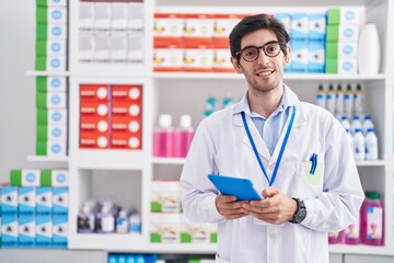 Young hispanic man pharmacist using touchpad working at pharmacy