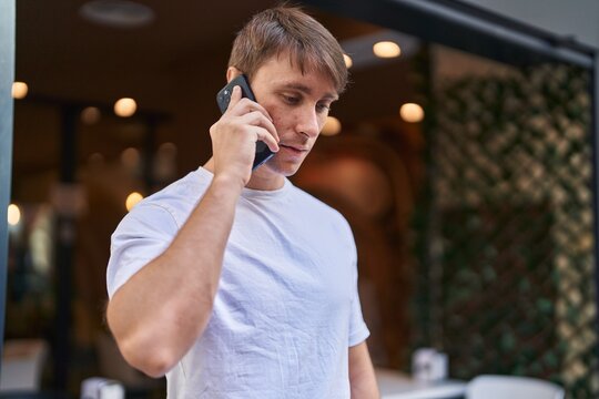 Young caucasian man talking on smartphone with serious expression at coffee shop terrace