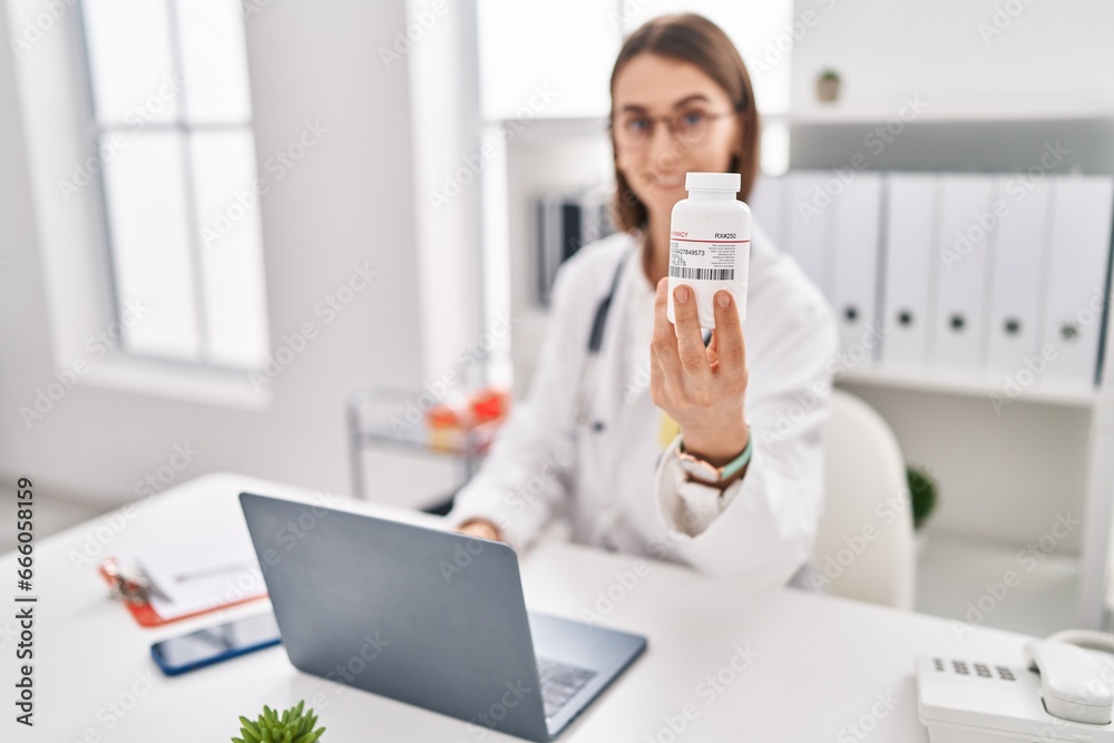 Wall mural young caucasian woman doctor using laptop holding pills at clinic