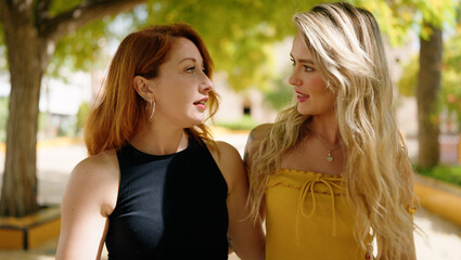 Fototapeta premium Two women hugging each other speaking and walking at park