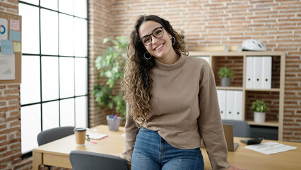 Young beautiful hispanic woman business worker smiling confident sitting on table at office