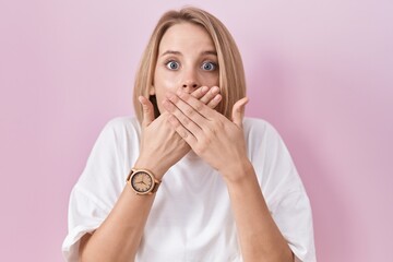 Young caucasian woman standing over pink background shocked covering mouth with hands for mistake....