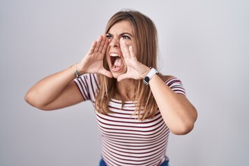 Young hispanic woman standing over isolated background shouting angry out loud with hands over mouth