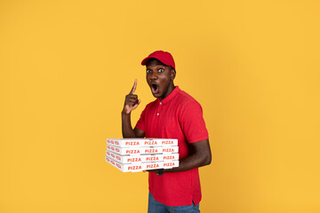 Shocked millennial black guy courier with open mouth hold many pizza boxes, point finger up to free...