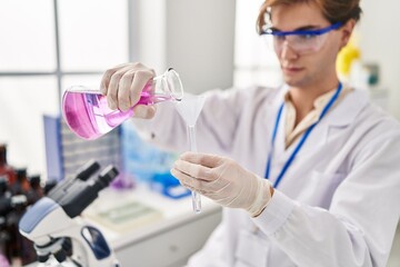 Fototapeta premium Young caucasian man scientist pouring liquid on test tube at laboratory